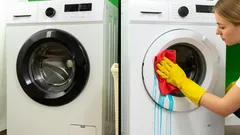 Nainen puhdistaa pesukoneen oven keltaisilla käsineillä ja punaisella liinalla.
